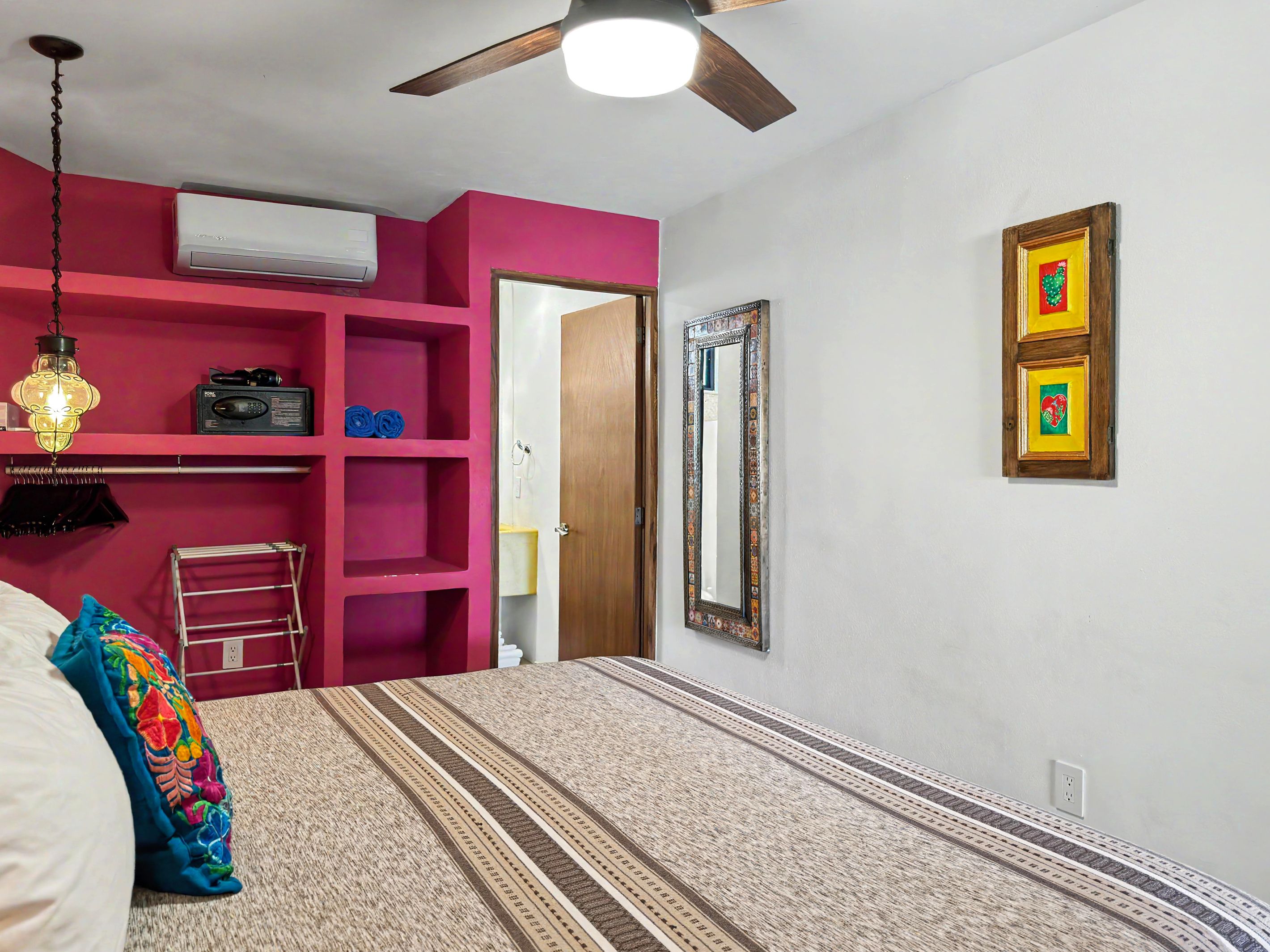 Un dormitorio con cama, ventilador de techo, estante con un radio y puerta que da a otra habitación.