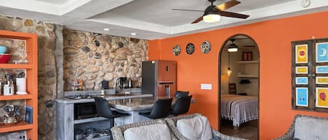 Una cocina moderna con pared de piedra, un comedor con muebles de mimbre y una sala de estar con paredes naranjas y ventiladores de techo.