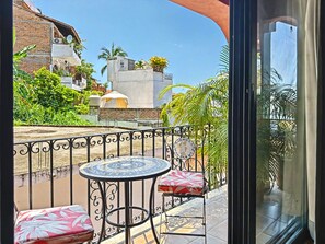 A balcony with a round table and chairs, a view of the surrounding buildings, and a clear sky.