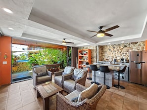 An open-plan living area with a kitchen, outdoor seating, and a ceiling fan.