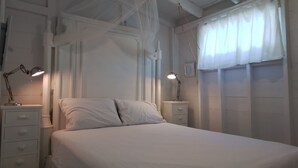 Une chambre à coucher avec un lit, deux tables de chevet avec des lampes, une fenêtre avec des rideaux légers et un baldaquin au-dessus du lit.