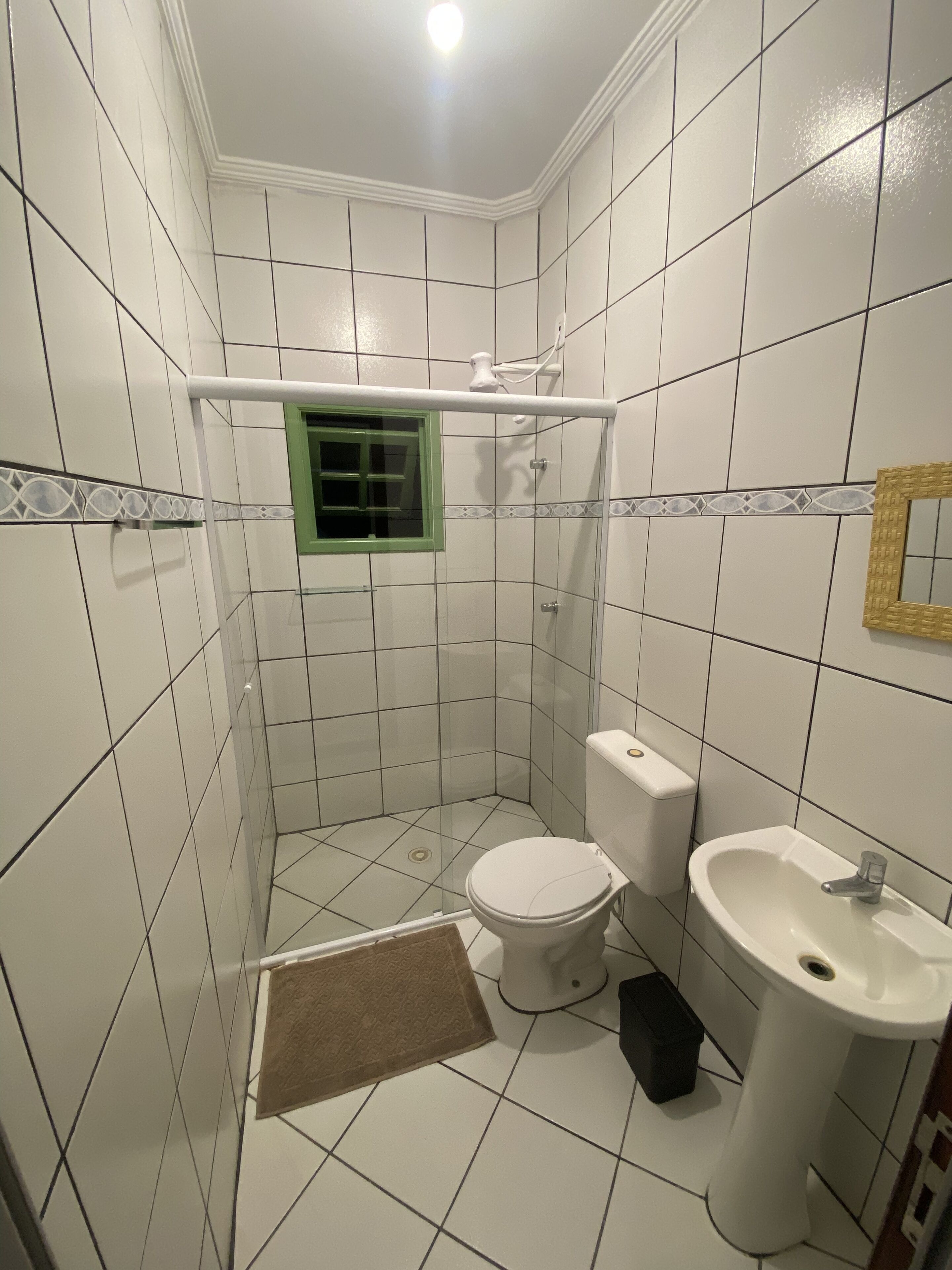 Casa de banho pequena, com azulejos, sanita, lavatório e cabine de duche.