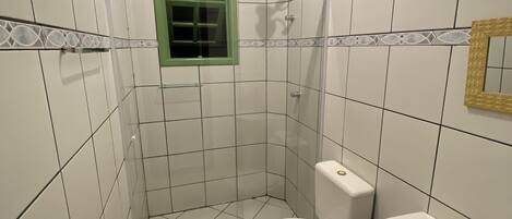 Casa de banho pequena, com azulejos, sanita, lavatório e cabine de duche.