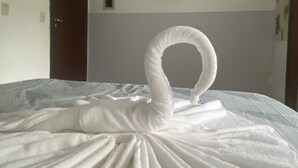 A neatly made bed with a towel arranged in the shape of a swan. - Pousada Meraki Beach (Caraguatatuba)