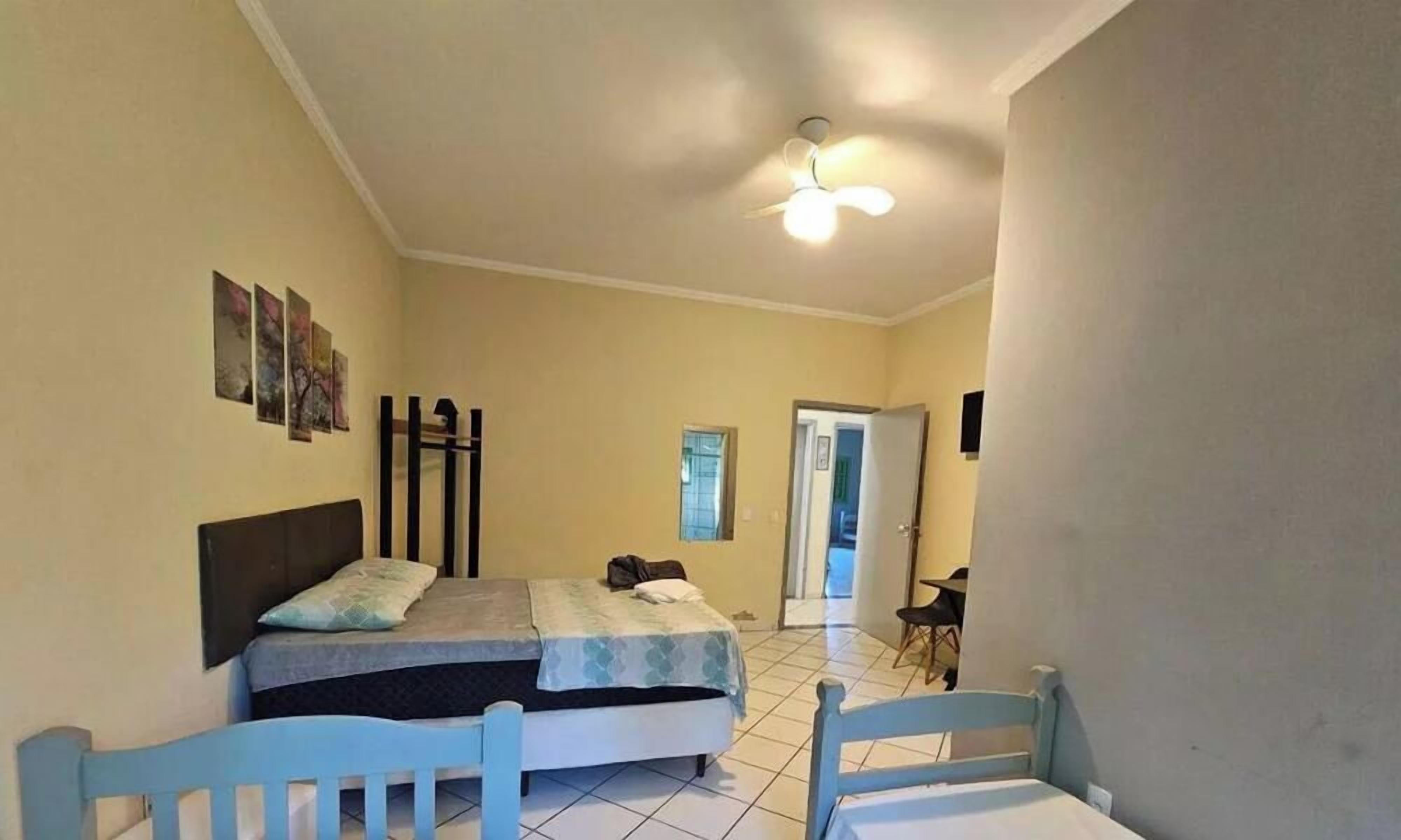 Un dormitorio con cama, una silla, ventilador de techo y puerta que da a otra habitación.
