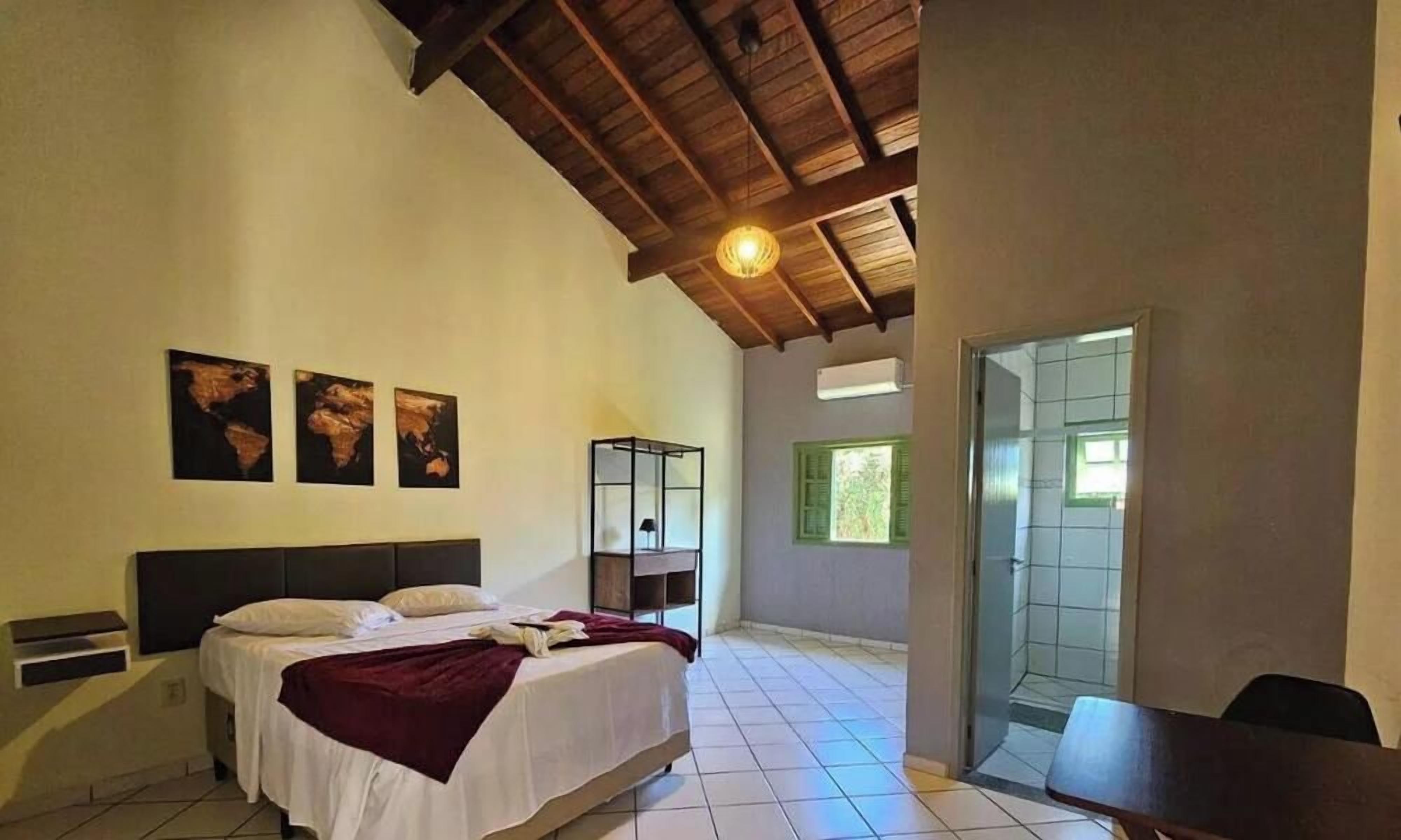 A bedroom with a bed, a nightstand, a desk, and a window.