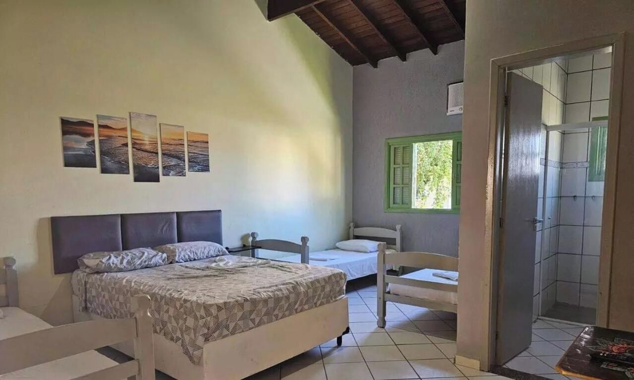 Un dormitorio con cama, una cama adicional, una silla y una ventana con persianas verdes.