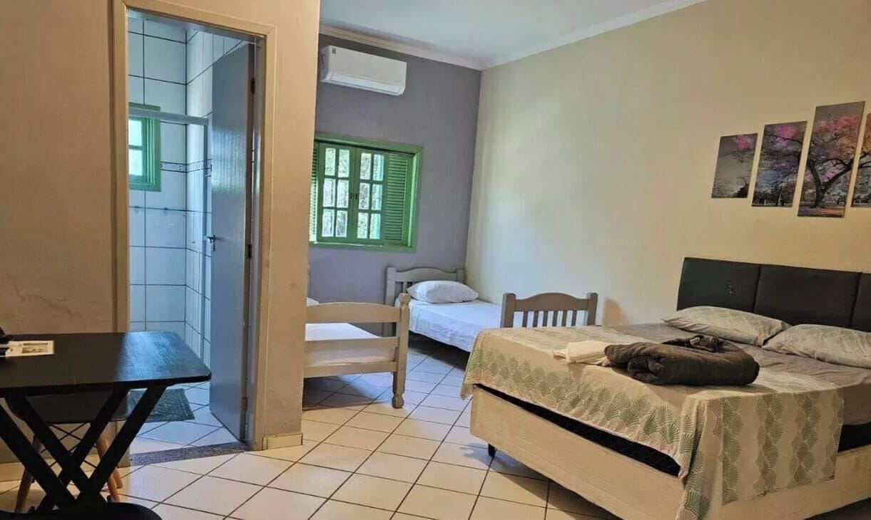 A bedroom with a bed, a chair, a table, and a window with shutters.