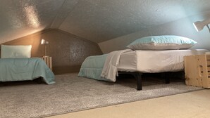 Quarto de sótão pequeno e acolhedor, com duas camas de solteiro, cabeceira de madeira e teto inclinado.