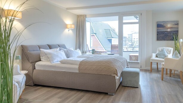 Une chambre moderne avec un grand lit, un coin salon avec des fauteuils et une vue sur l’extérieur.
