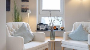 Un salon moderne avec deux canapés blancs, une petite table ronde et une fenêtre laissant entrer la lumière naturelle.