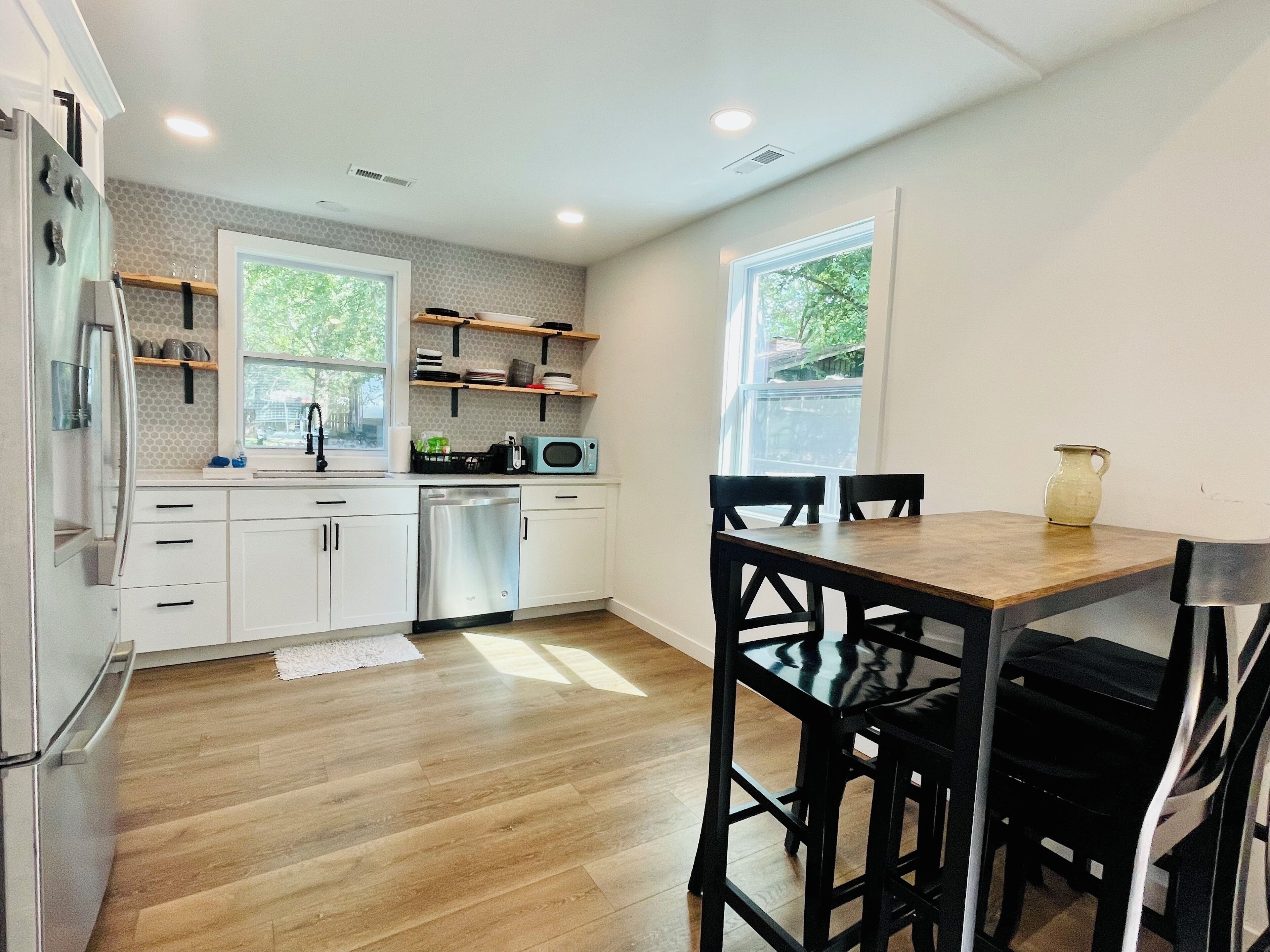 A modern kitchen with white cabinets, a stainless steel dishwasher, and a wooden dining table with black chairs.