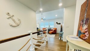 A spacious living area with a wooden floor, a white staircase with a rope railing, and a large anchor decoration on the wall. - Lakefront Home w/ Dock on Old Hickory Lake (Gallatin)