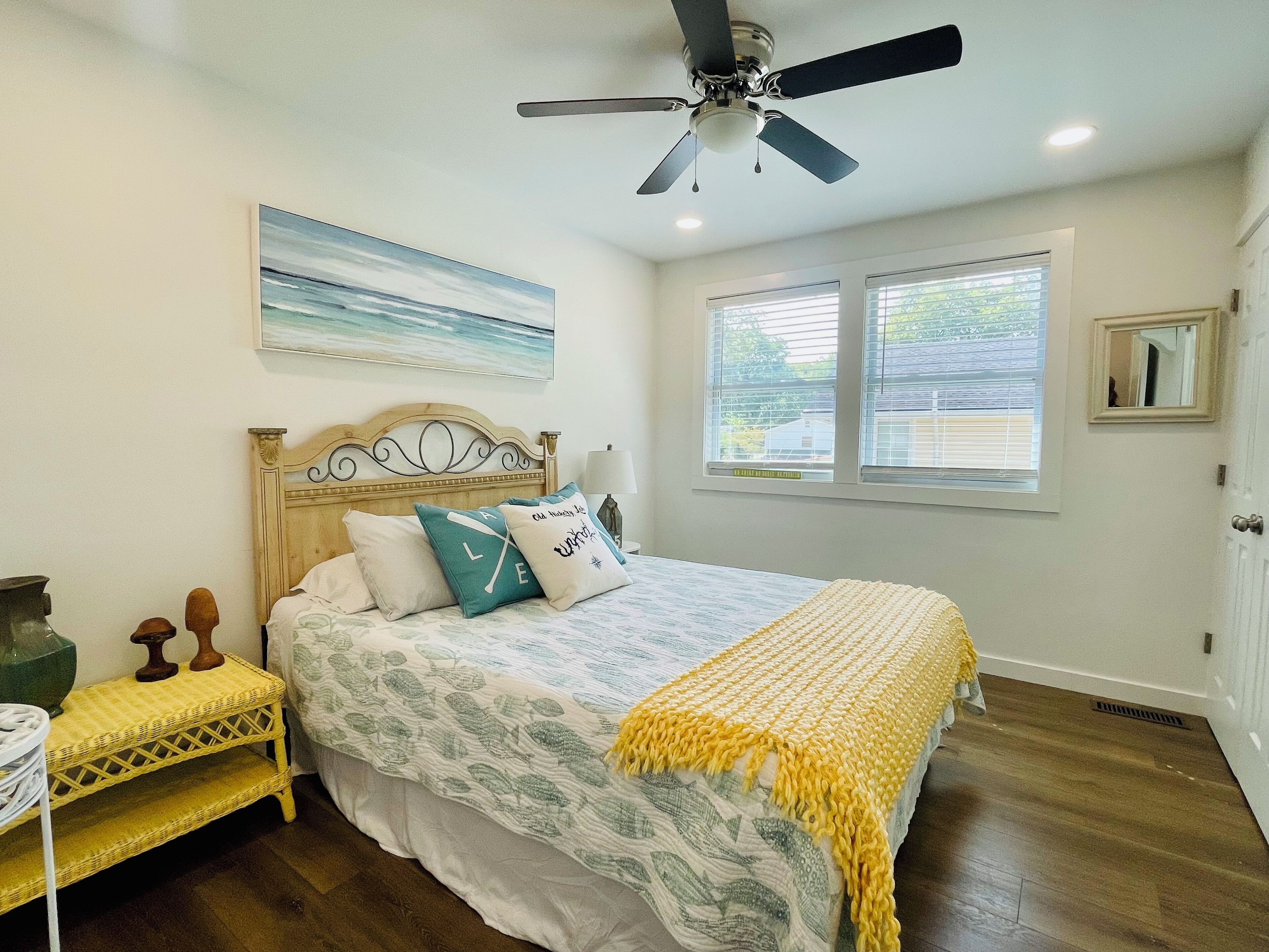 Une chambre à coucher avec un lit, un ventilateur de plafond, une fenêtre et un tableau accroché au mur.