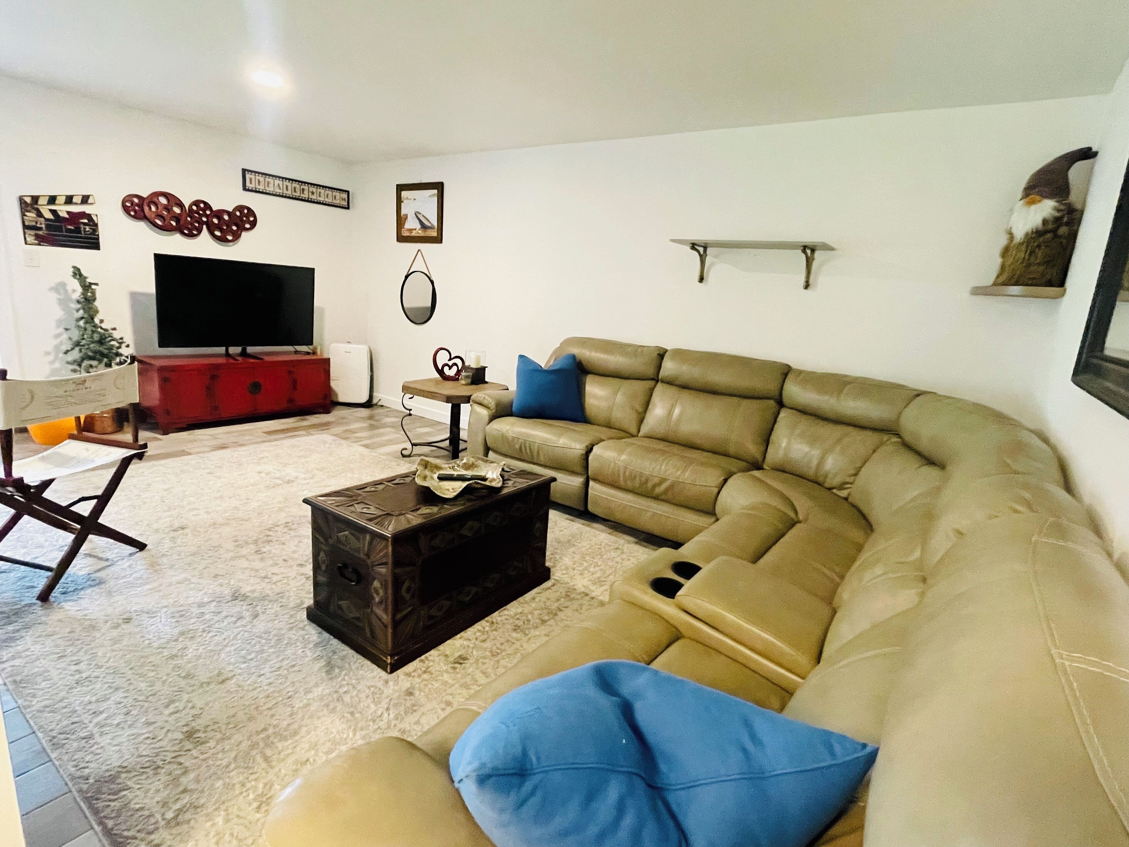 A living room with a brown leather sofa, a coffee table, a flat-screen TV, a red cabinet, and a small table with a mirror and decorative items.