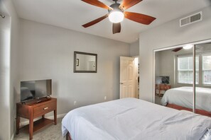 Ein Schlafzimmer mit Bett, Fernseher auf einem Holztisch, Deckenventilator und Spiegel.
