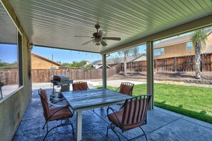 Eine überdachte Terrasse mit Tisch und Stühlen, einem Deckenventilator und Blick auf einen Hinterhof mit Holzzaun und einem Haus.