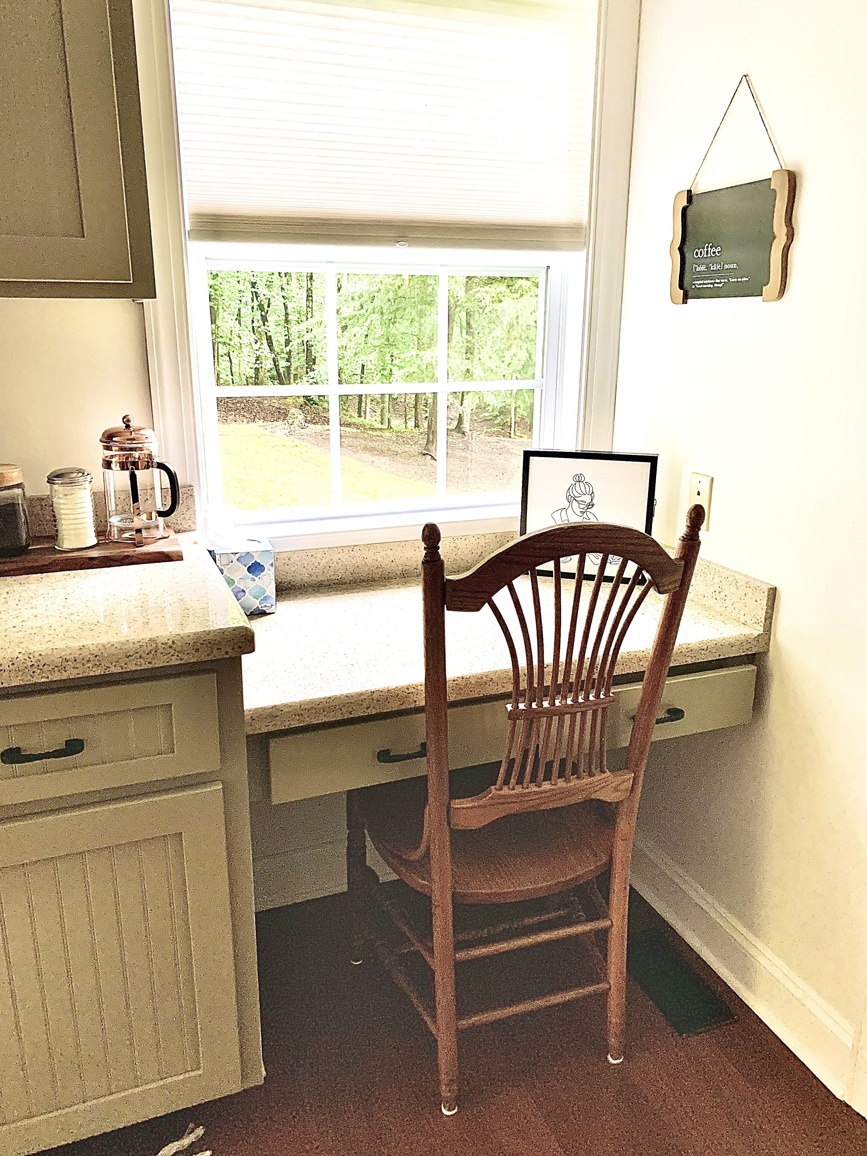 A kitchen with a wooden chair, a window with a view of trees, and a coffee maker on the counter.