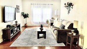 A living room with a television, sofa, coffee table, and decorative plants. - The Relaxing Oaks (Columbus)