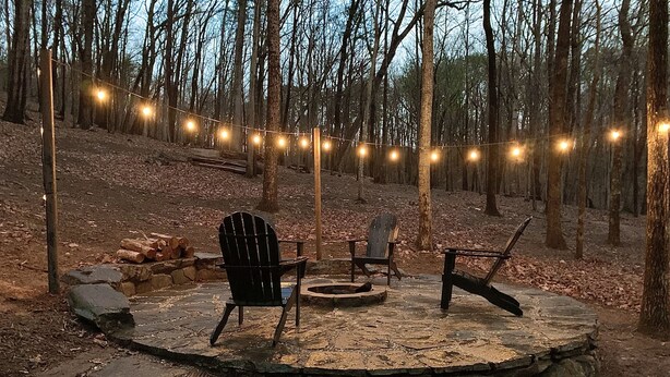 A circular stone deck with two Adirondack chairs and a fire pit, surrounded by a forest. - The Relaxing Oaks (Columbus)