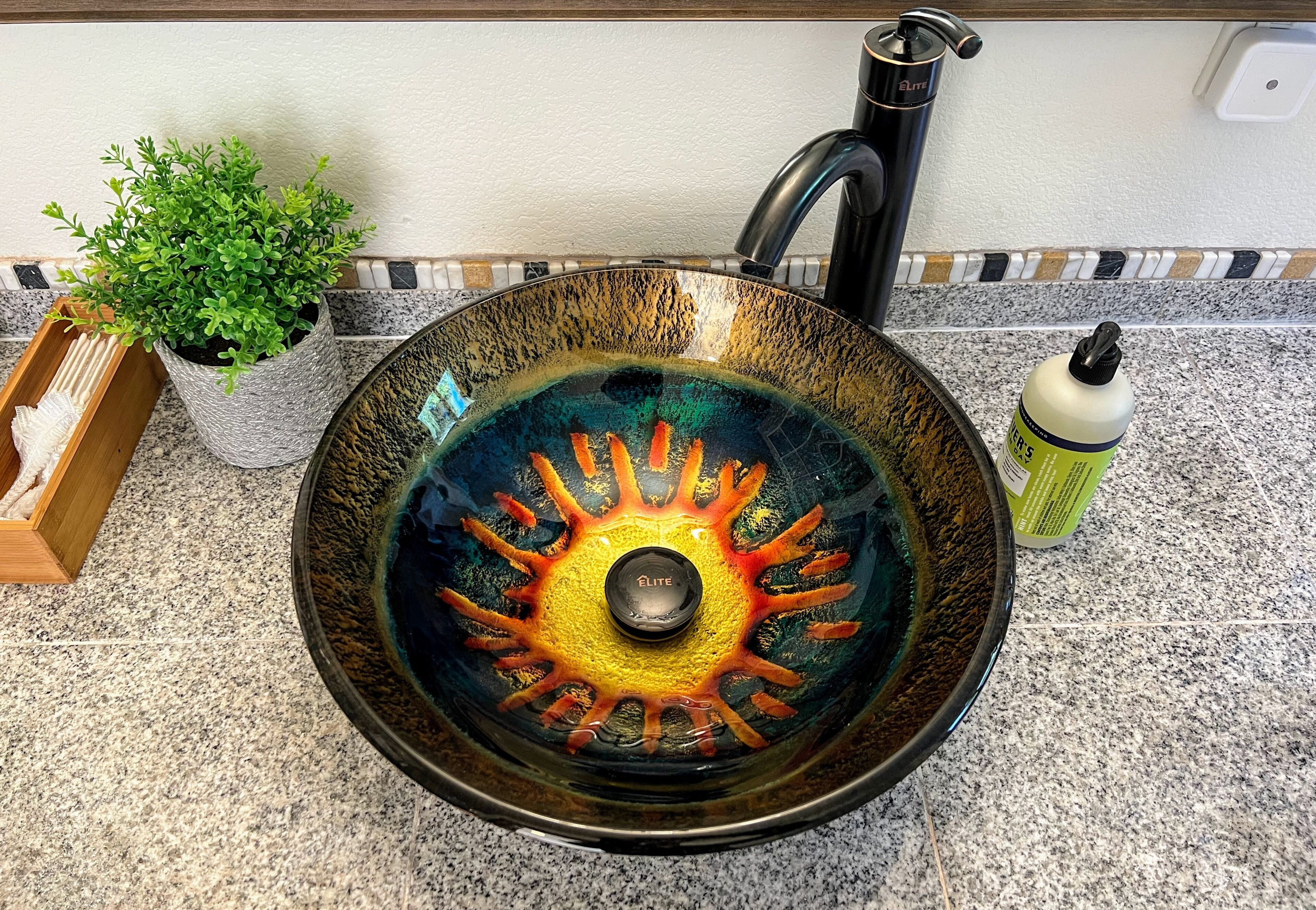 A kitchen sink with a decorative glass cover, a potted plant, and a bottle of dish soap.
