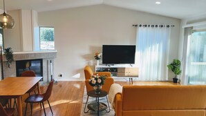 Een moderne woonkamer met een houten eettafel, een oranje bank en een flatscreen televisie.