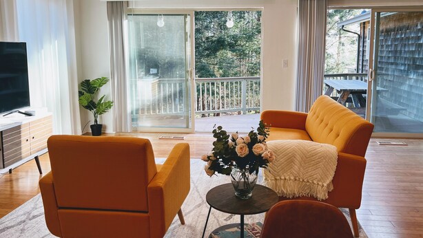 Een woonkamer met een bank, stoelen, een televisie en uitzicht op een terras en bomen.