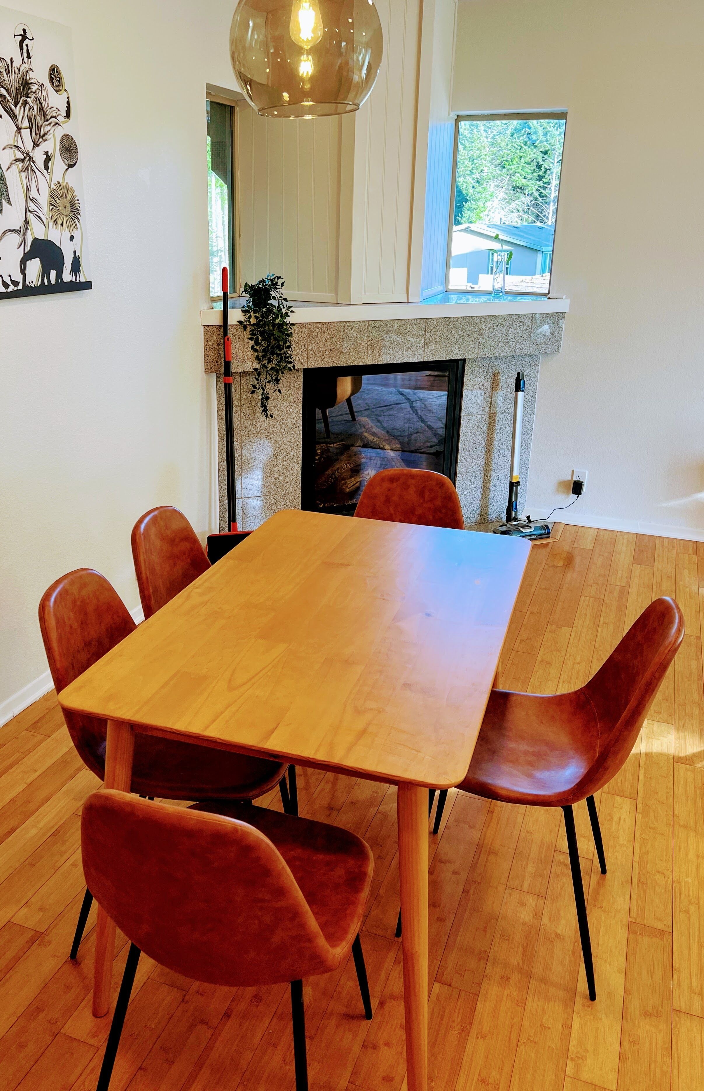 A dining area with a wooden table and six velvet chairs, a fireplace, and a window with a view of trees.