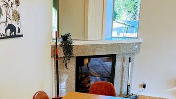 A dining area with a wooden table and six velvet chairs, a fireplace, and a window with a view of trees.