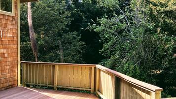 A wooden deck with a wooden railing, surrounded by dense trees.