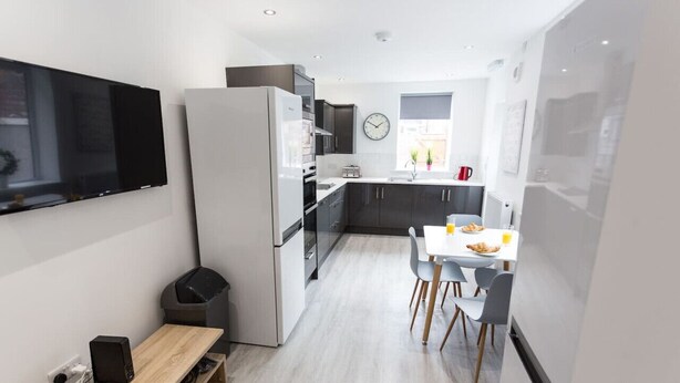 Una cocina moderna con horno empotrado, refrigerador y comedor con mesa y sillas.