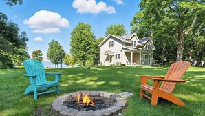 Een huis met een vuurkuil in de voortuin, twee Adirondack-stoelen en een meer op de achtergrond.