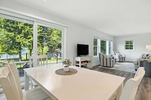Un vaste espace de vie comprenant une grande fenêtre, un téléviseur, des fauteuils à rayures et une table à manger avec des chaises.