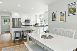 Une cuisine moderne avec des meubles blancs, des appareils en acier inoxydable et un coin repas comprenant une table et des chaises blanches.