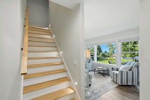 A staircase with wooden steps leading to a living area with a view of greenery outside.