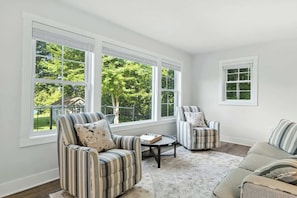 A room with large windows, two striped armchairs, a small round table, and a sofa.