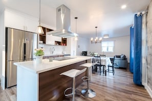 A modern kitchen with a central island, stainless steel appliances, pendant lighting, and a dining area with a table and chairs.