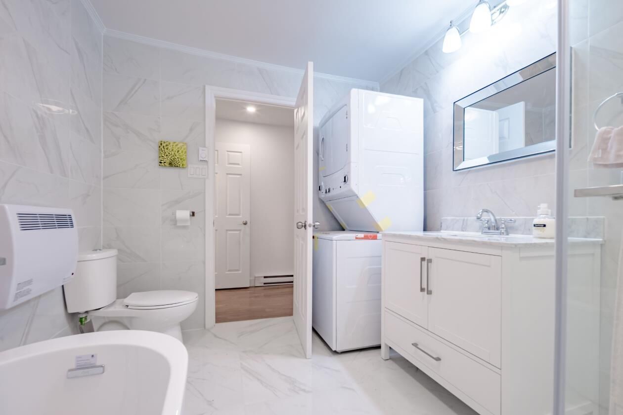 Une salle de bain moderne équipée de toilettes, d’un lave-linge, d’une baignoire et d’un meuble-lavabo avec un miroir.