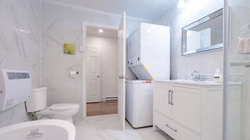 Une salle de bain moderne équipée de toilettes, d’un lave-linge, d’une baignoire et d’un meuble-lavabo avec un miroir.