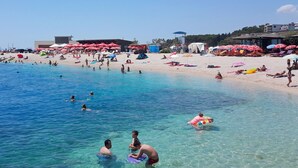 Una platja amb aigua cristal·lina, persones nedant i prenent el sol, i para-sols de platja.