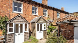 A brick house with two small sheds, a chimney, and a clear blue sky. - A cozy cottage on the North Norfolk coast (Brancaster Saithe)