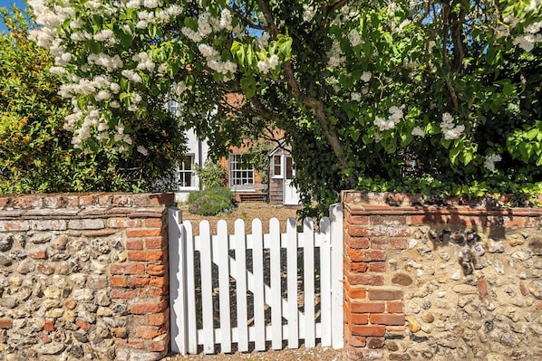 A stone wall with a white picket fence, a brick wall, and a tree with white flowers.