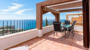 Ein Balkon mit Tisch und Stühlen, Blick auf das Meer und eine Pergola.