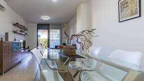 A modern dining area with a glass table, white chairs, a wooden cabinet, and a framed picture on the wall. - Vila del Far by Interhome (St Carles de la Ràpita)