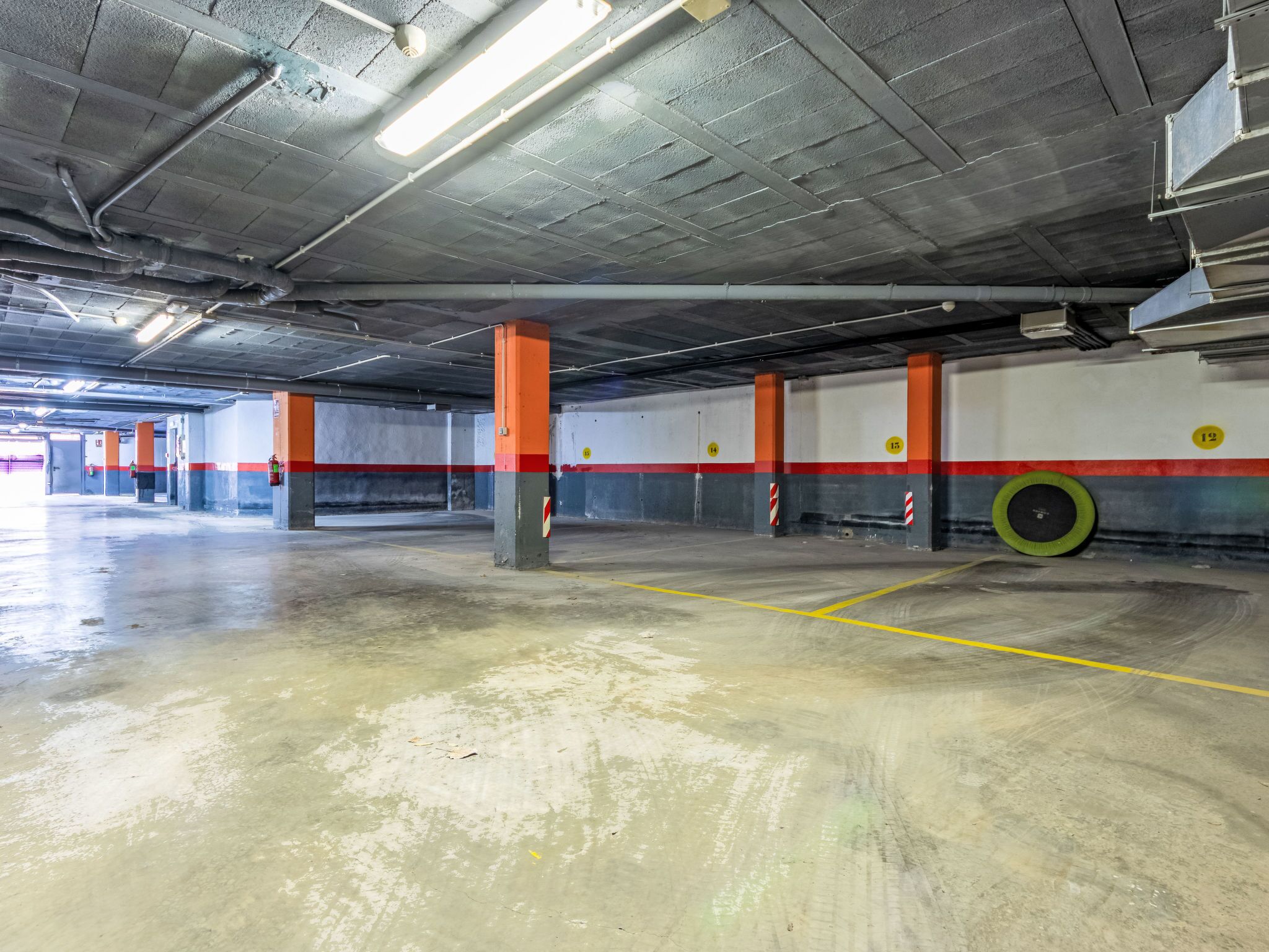 Een parkeergarage binnen met betonnen vloeren, oranje en grijze pilaren en gele parkeerlijnen.
