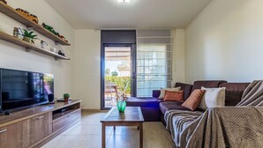 A living room with a TV, wooden shelves, a sofa, and a sliding glass door leading to a patio. - Vila del Far by Interhome (St Carles de la Ràpita)