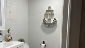 Une salle de bain avec des toilettes blanches, un lavabo avec un miroir et une décoration murale représentant une ancre.