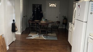 Une cuisine compacte avec un coin repas, un plancher en bois, des armoires blanches et un réfrigérateur blanc.