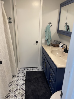 A bathroom with a white door, a sink with a mirror above it, a towel hanging on the wall, and a patterned floor.