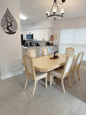 Un coin repas avec une table et des chaises en bois, un lustre et une cuisine en arrière-plan.